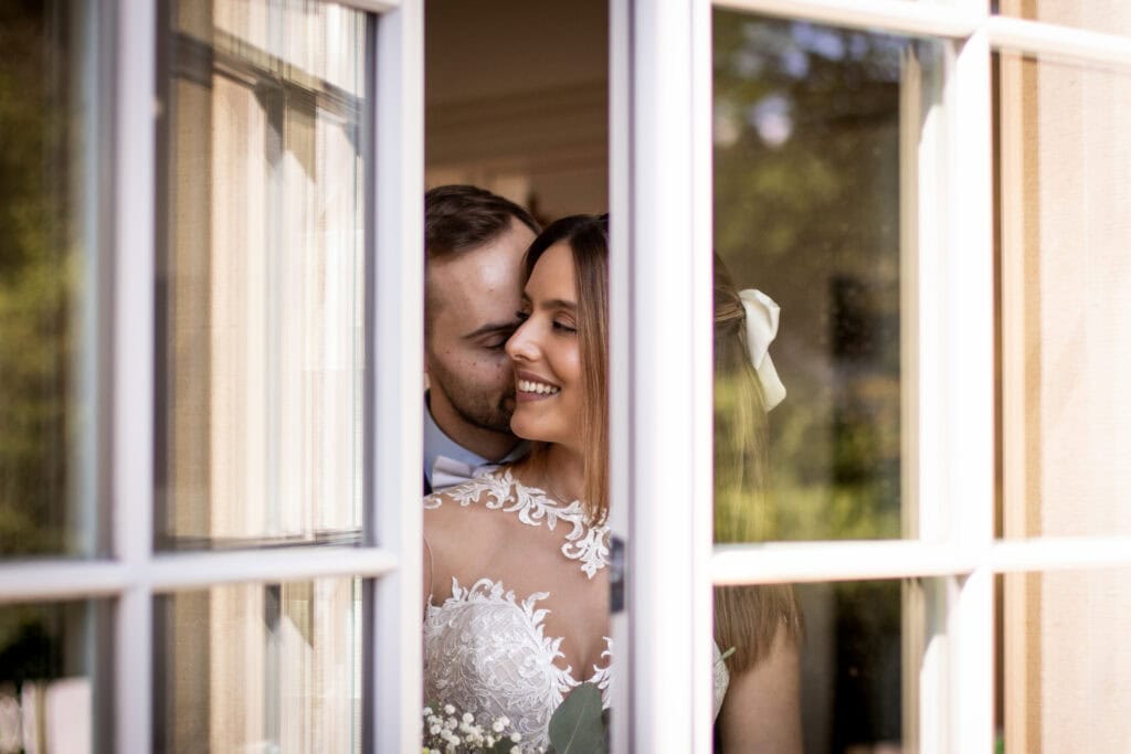 Glückliches Brautpaar bei der freien Trauung durch ein Fenster fotografiert.