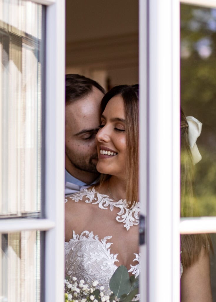 Hochzeitsfoto eines verliebten Paares, intime Momentaufnahme im Hochzeitsshooting durch das Fenster.