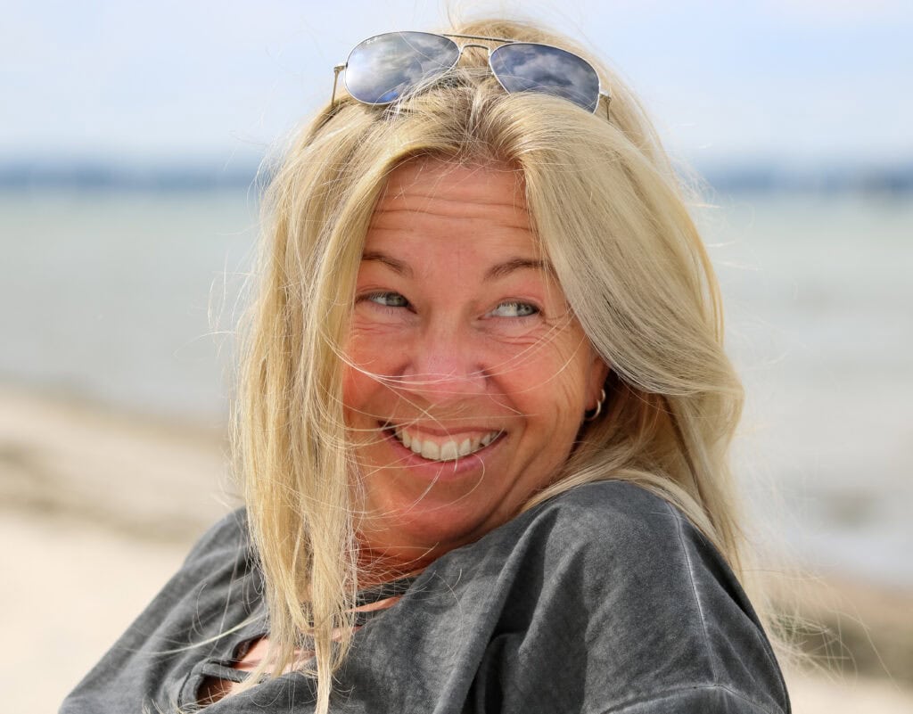 Hochzeitsfotografin Diane K. Senft im Selbstporträt. Mit Sonnenbrille im Haar am Strand, lachend und entspannt.