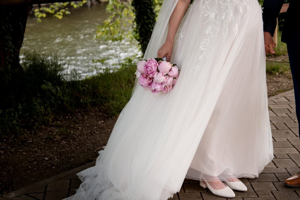 Hochzeitskleid mit Blumenstrauß am Flussufer, romantische Hochzeitsfotografie.