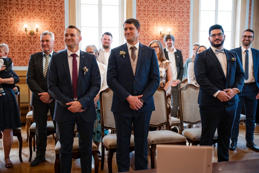 Bräutigam und Hochzeitsgäste im festlichen Saal des Standesamtes Fürstenfeldbruck während der Trauung, elegante Atmosphäre, glückliche Momente.