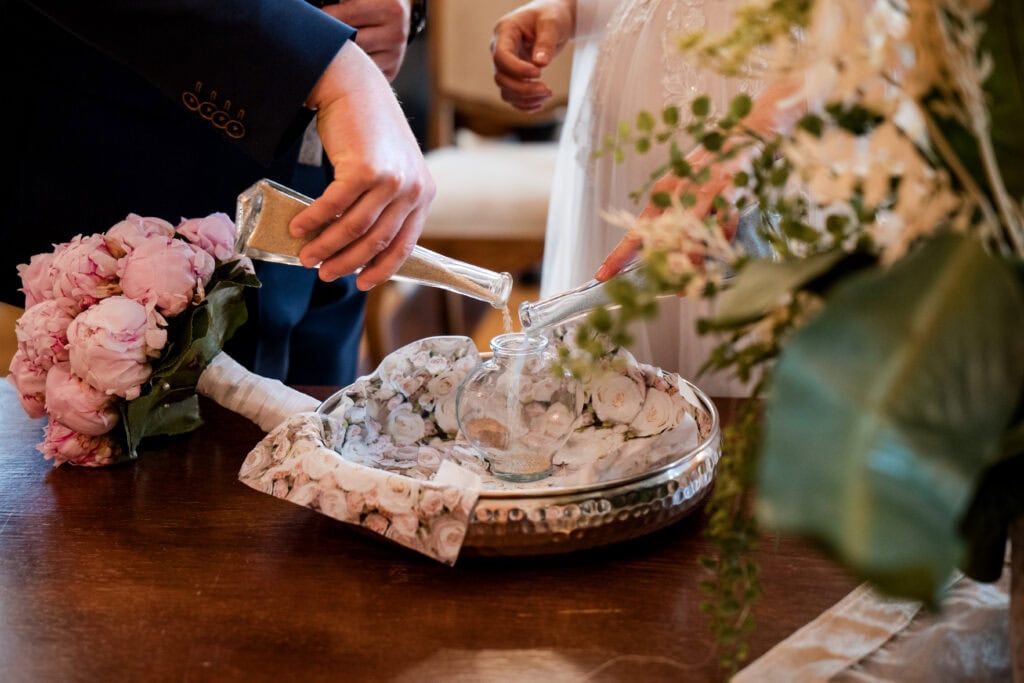 Braut und Bräutigam bei Sandzeremonie mit Blumenstrauß, romantischer Hochzeitsszene.