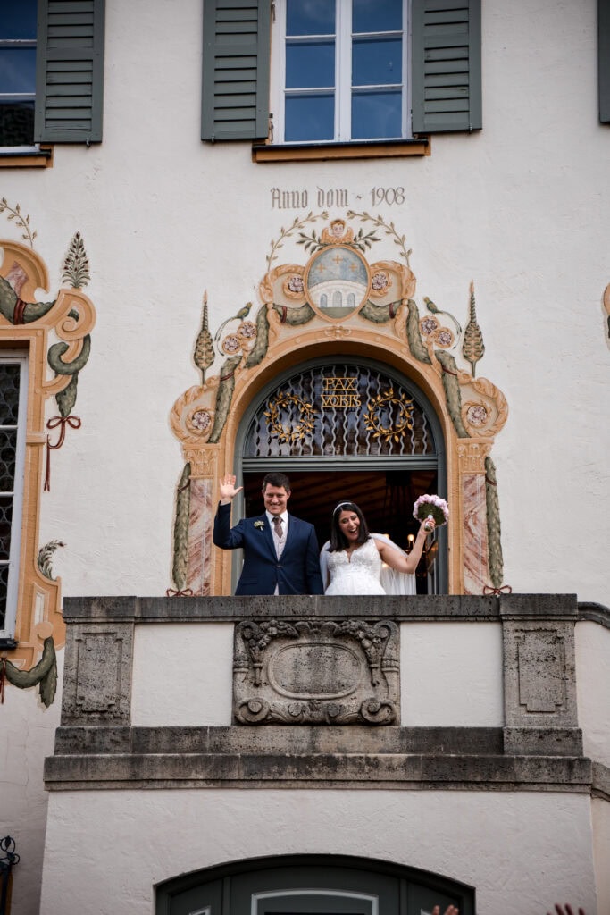 Hochzeitspaar vor kunstvoller, historischer Fassade mit barockem Dekor und Fensterläden.