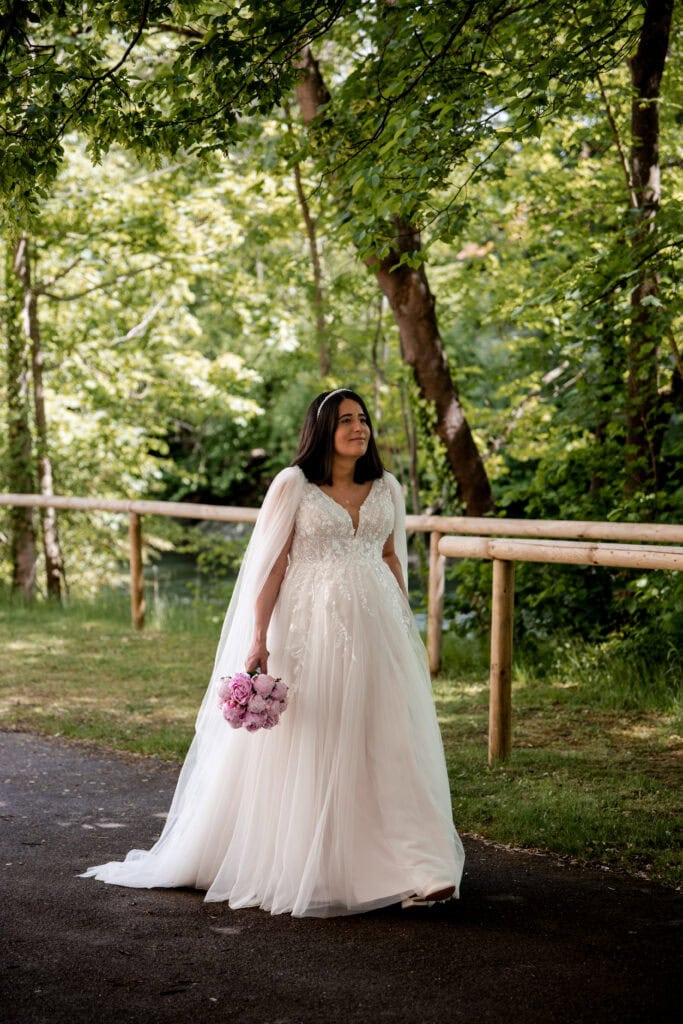Braut in weißem Hochzeitskleid mit Blumenstrauß im Park.