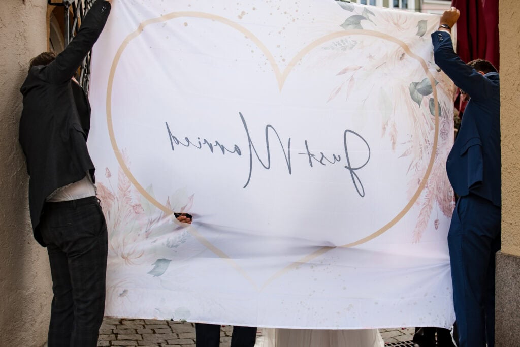 Hochzeitspaar hält Willkommensbanner mit Herz-Design, Hochzeitsfotografie.