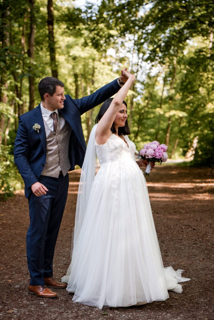 Braut und Bräutigam tanzen im Wald bei ihrer Hochzeit, umgeben von grünen Bäumen.