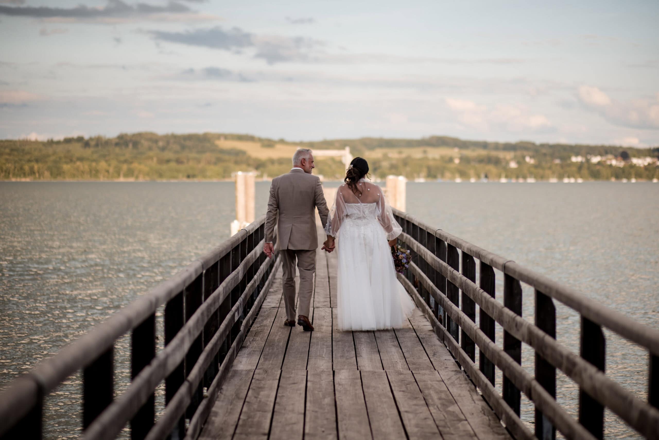 Braut und Bräutigam gehen Hand in Hand auf einem Steg am Ammersee. Hochzeitsfotografie Diane K. Senft