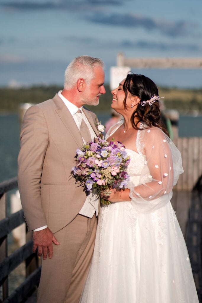 Braut und Bräutigam bei Hochzeit am Wasser, liebevolle Umarmung, Hochzeitsfotografie.