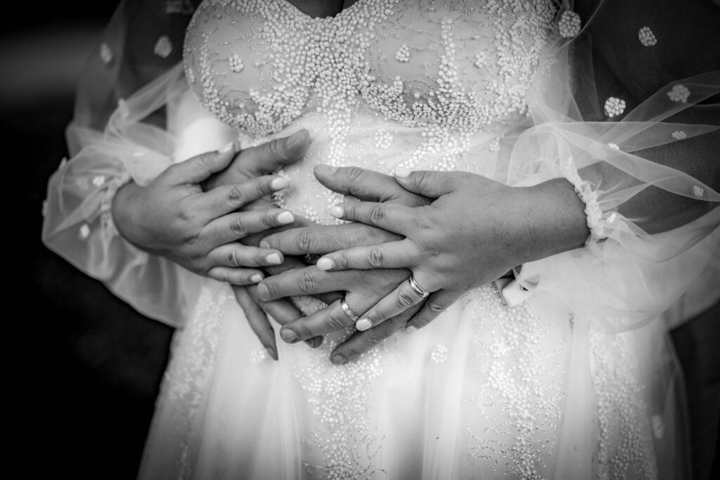 Hände eines Brautpaares in Herzform auf Brautkleid, emotionale Hochzeitsaufnahme.