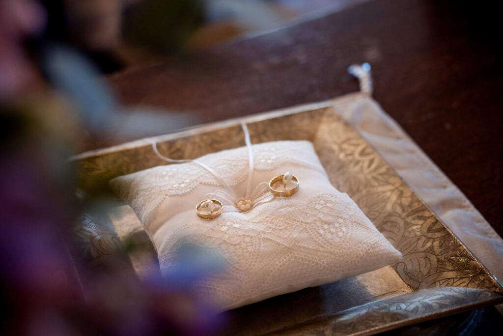 Hochzeitsringe auf einem weißen Kissen mit Spitze und Perlen.